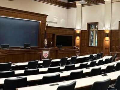 Wood-paneled courtroom with a raised bench, American flag, and rows of empty seats