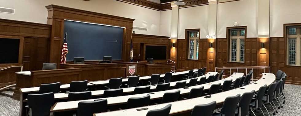 Wood-paneled courtroom with a raised bench, American flag, and rows of empty seats